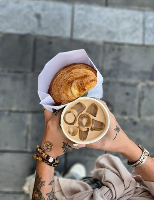 Hands ho9lding a croissant and iced coffee
