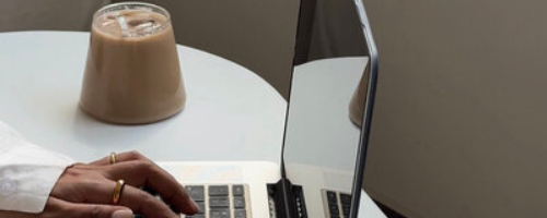 hands on a laptop keyboard with iced coffee