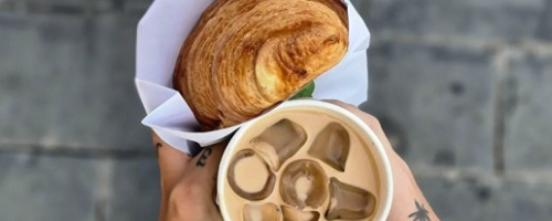 Hands ho9lding a croissant and iced coffee